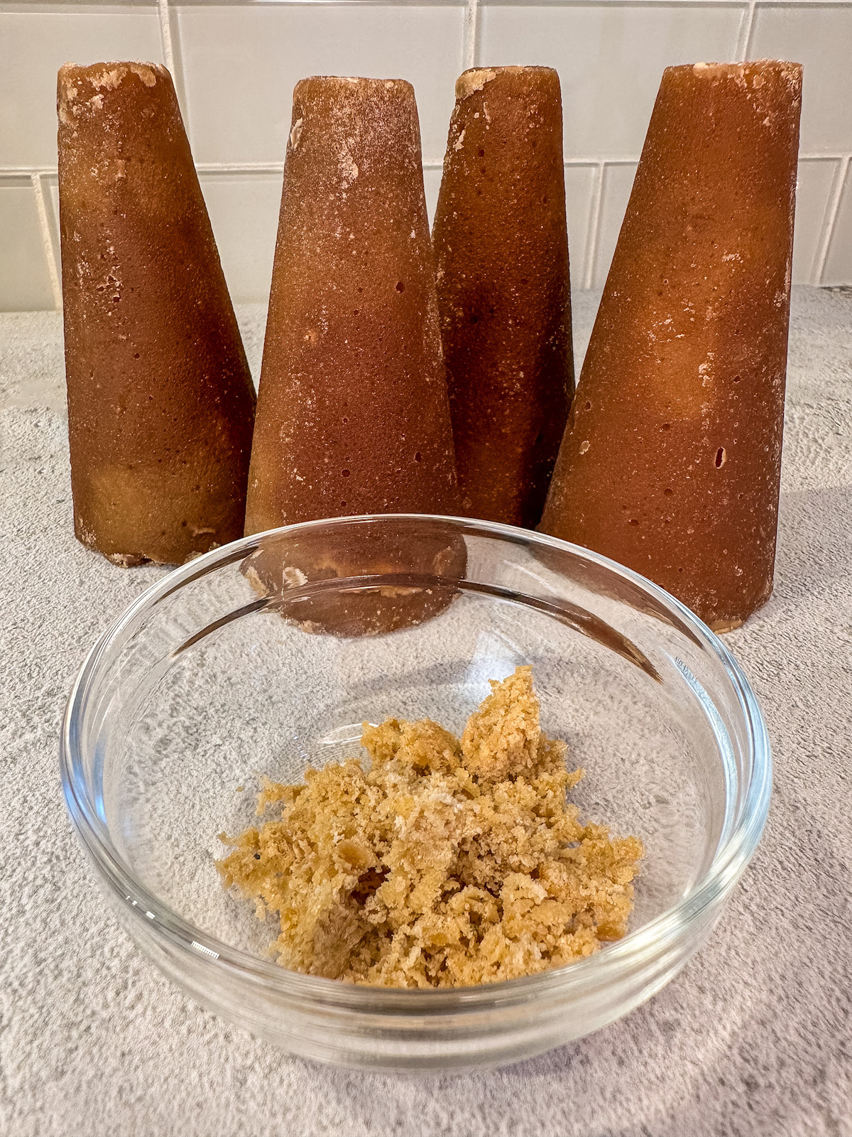 Four Piloncillo sugar cones behind a bowl of grated Piloncillo.