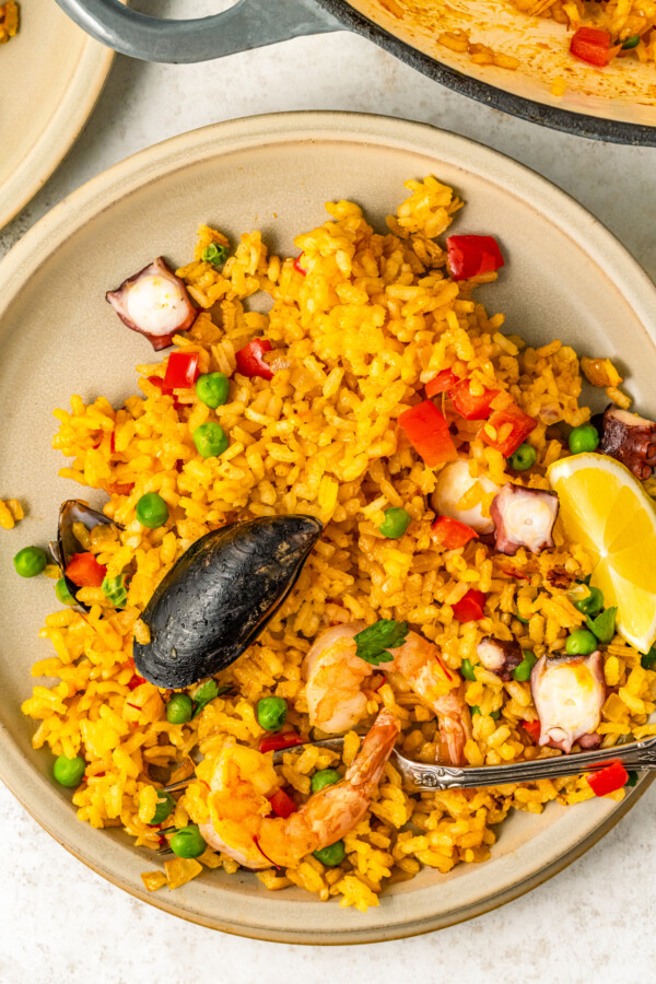A plate of Spanish seafood rice cooked with saffron and vegetables with a fork about to take a bite.