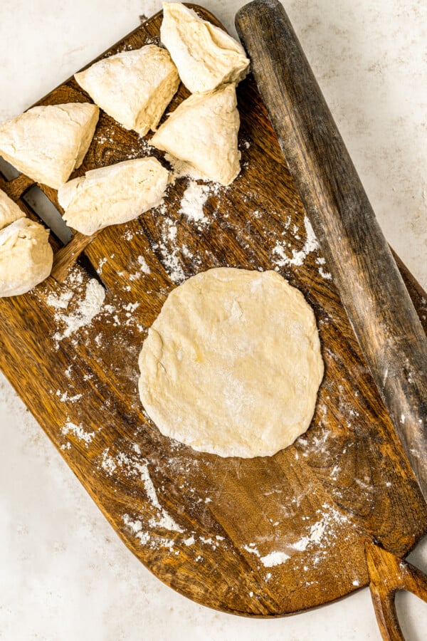 Flattening the dough into a round disk shape with a rolling pin.