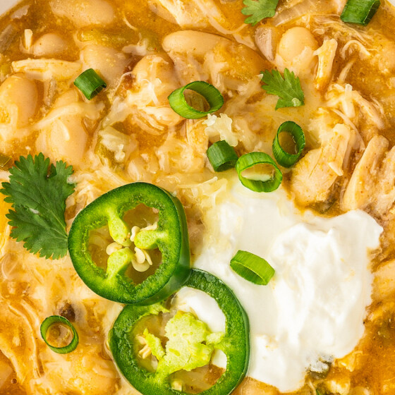 Up close image of a bowl of creamy white chicken chili topped with sour cream, cilantro, green onions and sliced jalapeños.
