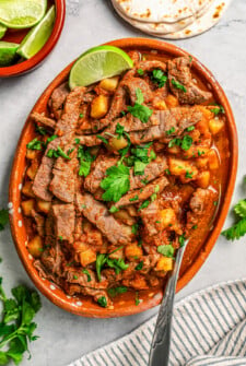 Juicy and spicy Bistec Ranchero with potatoes served on a large serving platter with fresh cilantro on top and lime wedges on the side.
