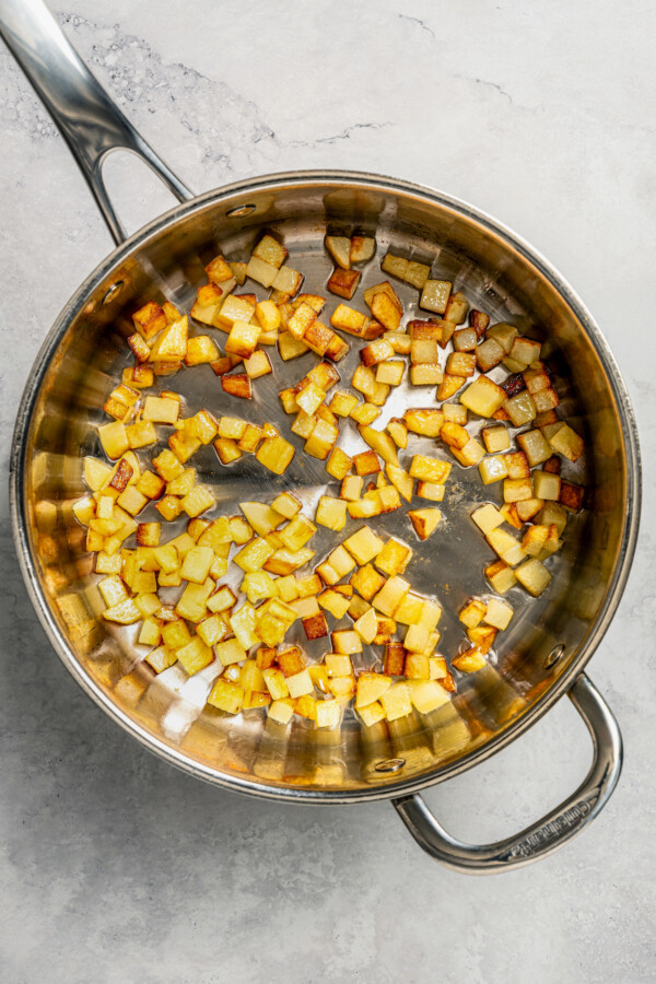 Cubed potatoes being browned in a skillet with oil.