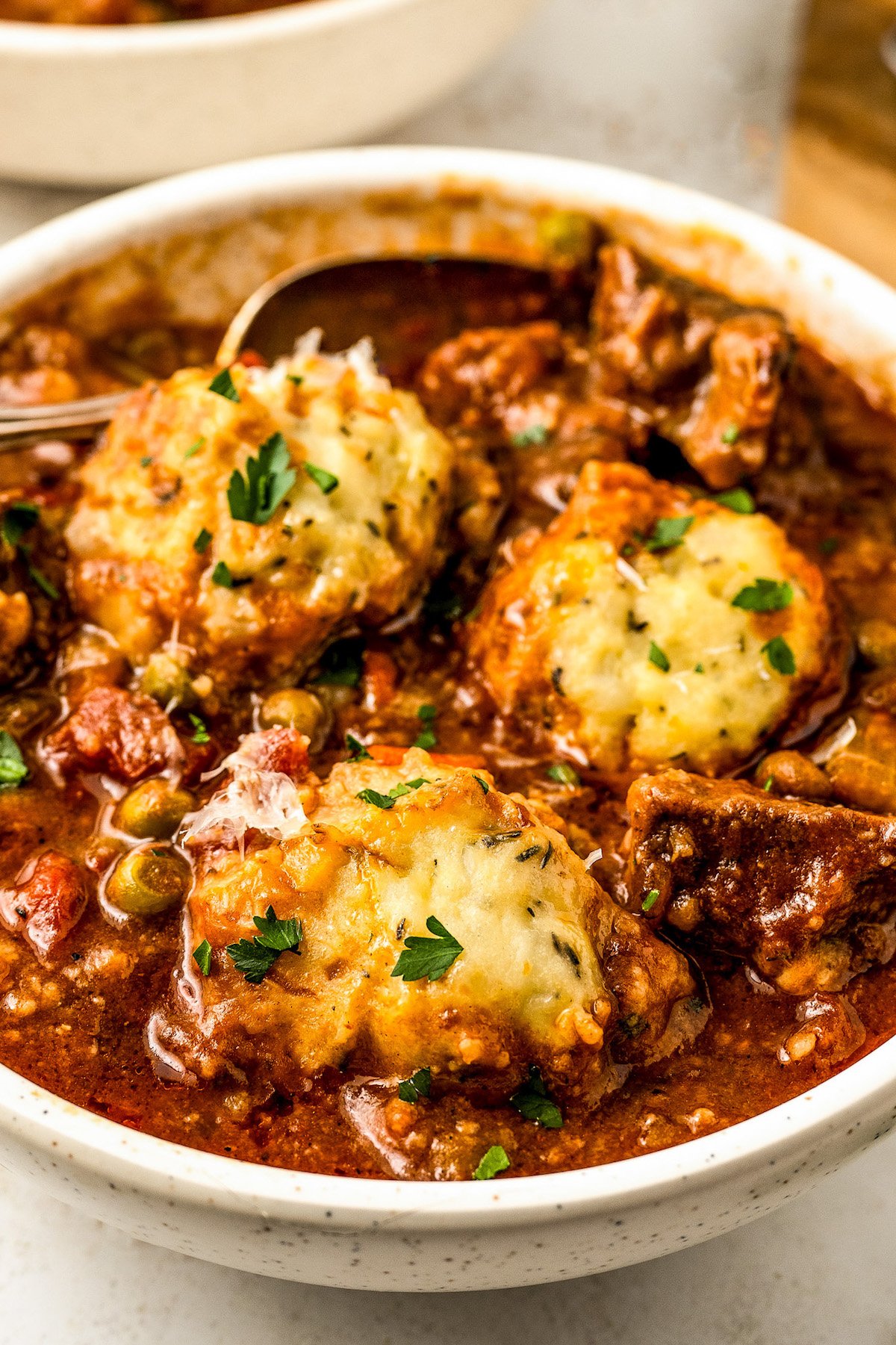 Hearty beef stew recipe with cheesy potato dumplings in a bowl topped with fresh parsley and grated parmesan cheese.