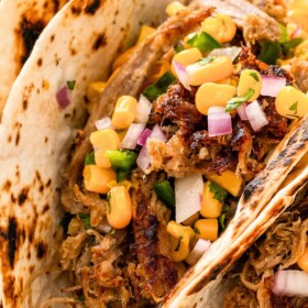 Three slow cooker carnitas tacos topped with fresh corn salsa and cilantro.