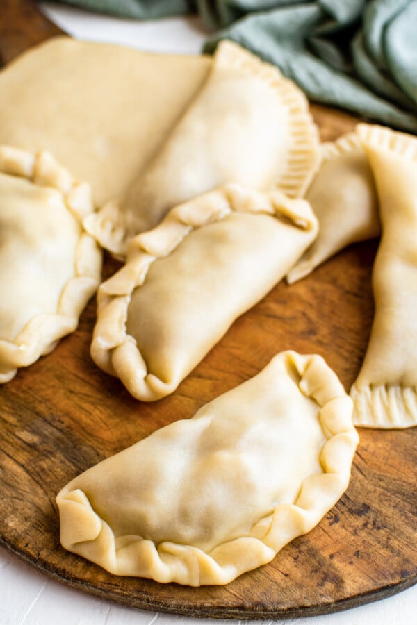 Stuffed empanada dough folded into empanada shapes and arranged on a cutting board.