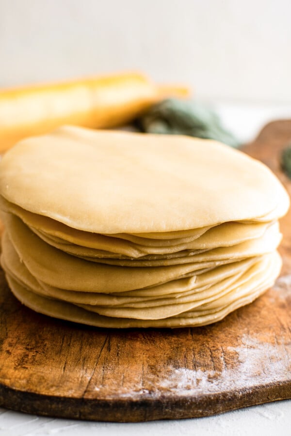 Disks of homemade empanada dough stacked on top of each other after being rolled flat with a rolling pin.