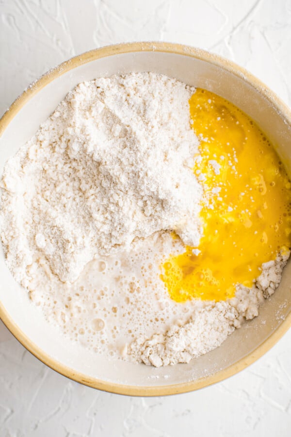 Egg and water being added to a bowl of flour, butter and salt.