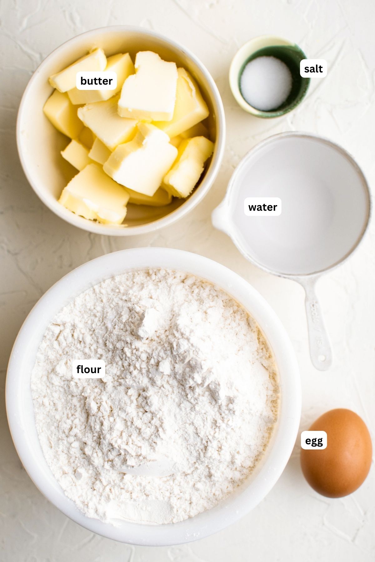Ingredients for empanada dough recipe arranged in bowls, from top to bottom: salt, butter, water, flour and egg.