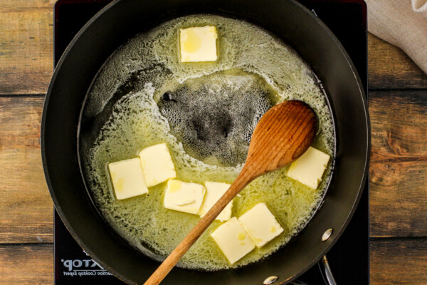 Butter being melted in a skillet with a wooden spoon.