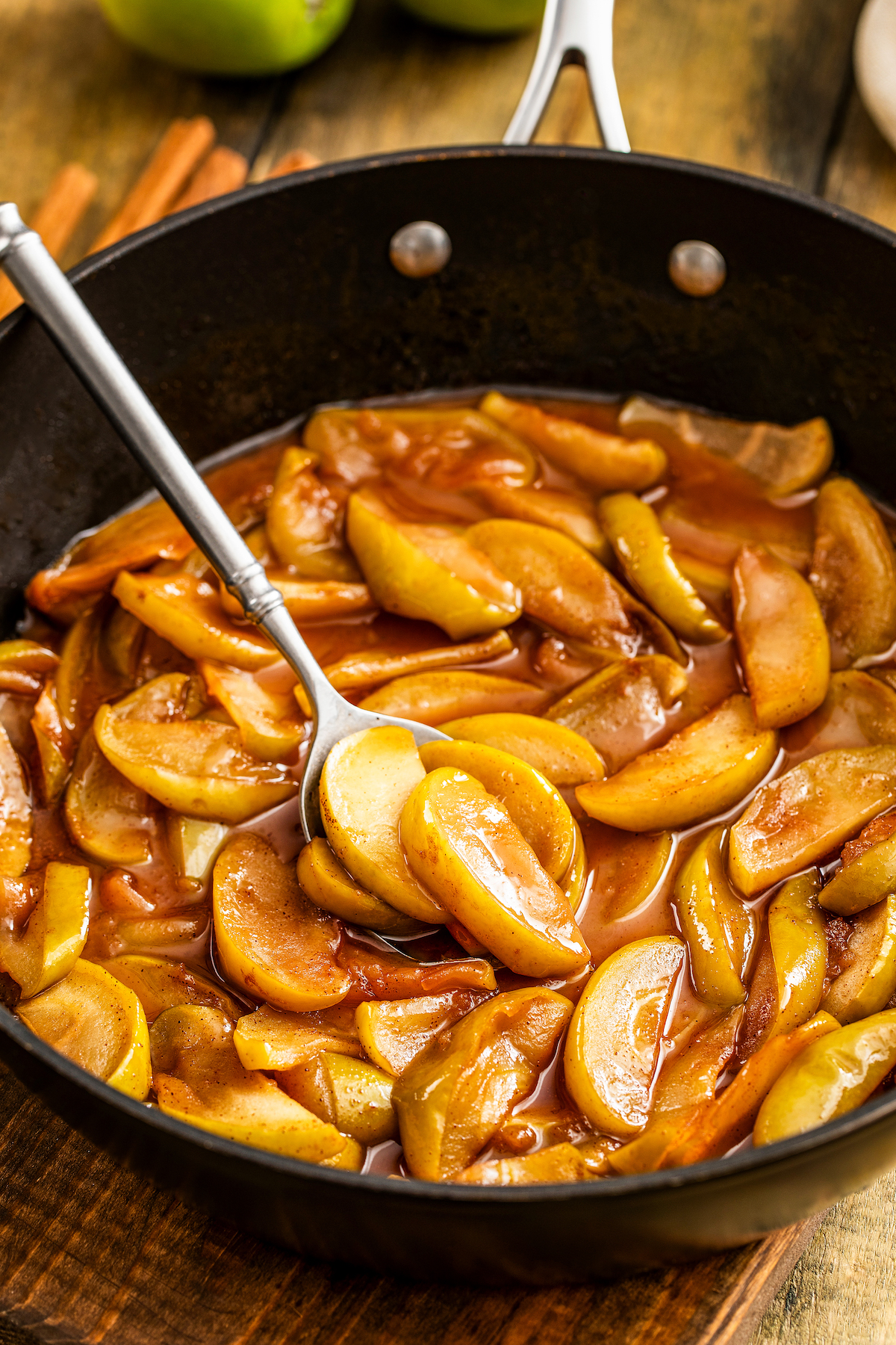 Showing how to make fried apples in a skillet with a spoon stirring the apples.