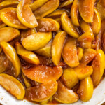 Cracker barrel fried apples in a bowl with cinnamon sticks on the side.