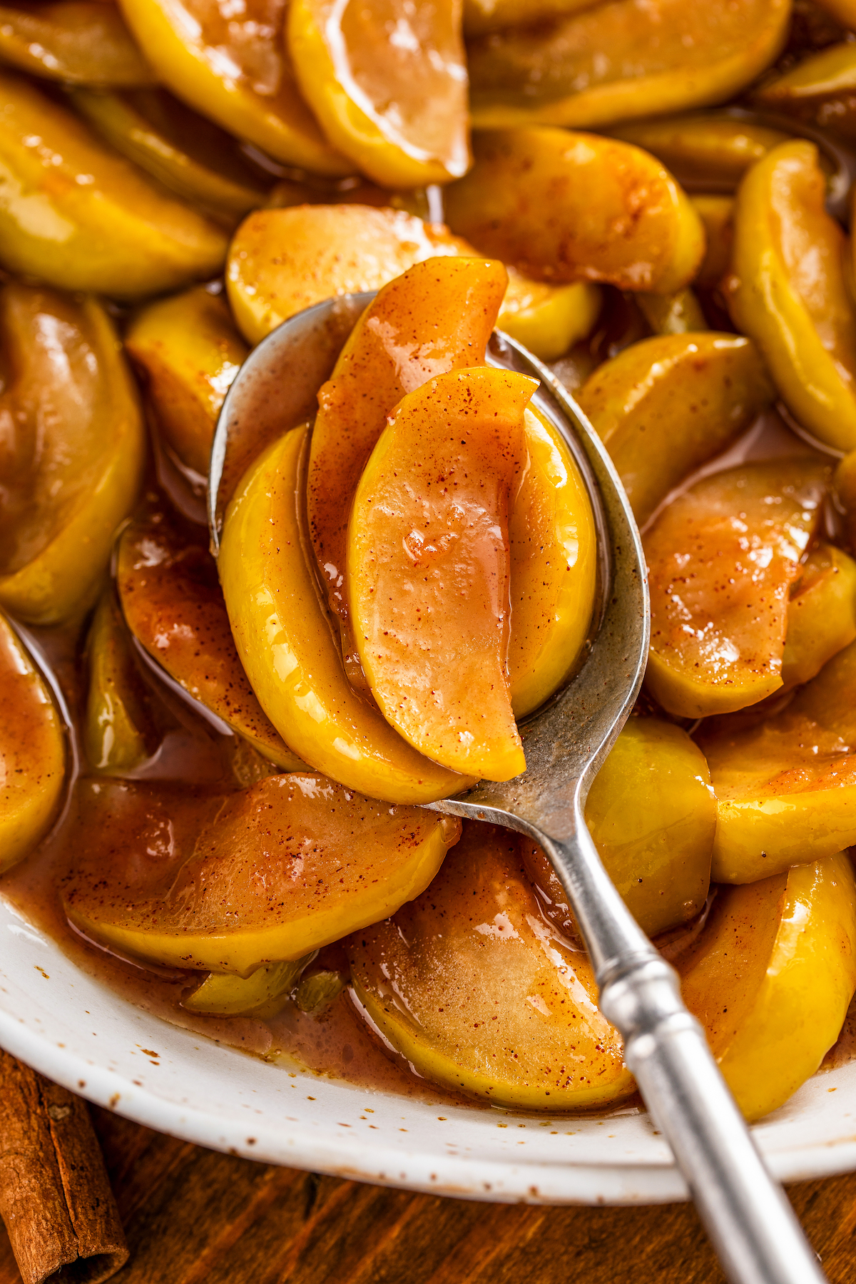 A spoonful of tender fried apples in a sweet cinnamon and brown sugar syrup being lifted out of a bowl.