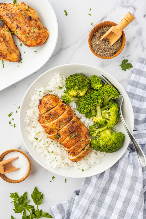 Juicy brown sugar chicken breast sliced into strips on top of a bed of white rice with a side of steamed broccoli.