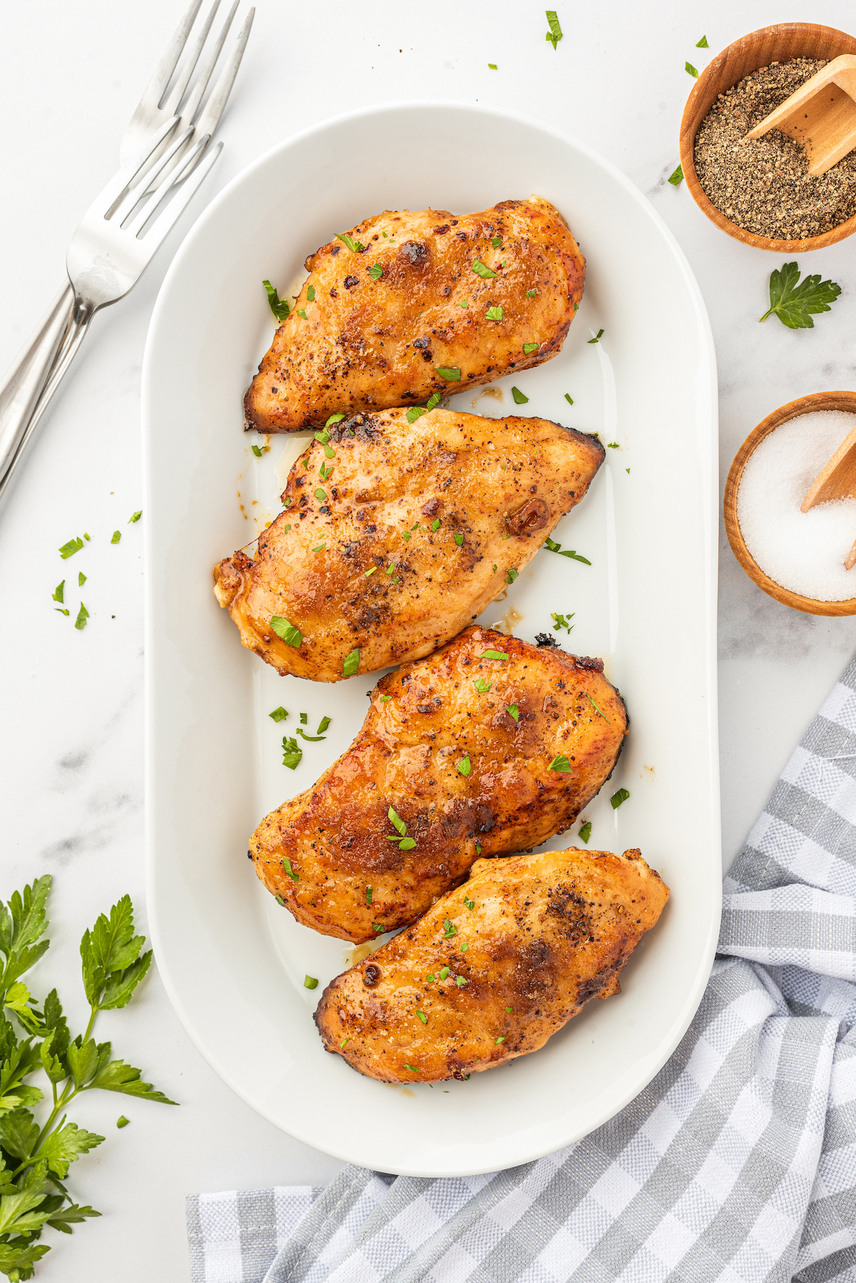 Four juicy brown sugar chicken breasts on a serving platter topped with fresh herbs.