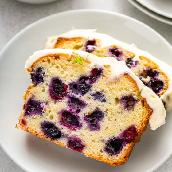 Two slices of lime blueberry pound cake with cream cheese frosting on top on a plate.