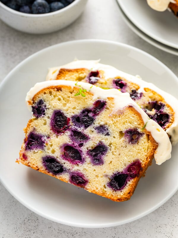 Two slices of lime blueberry pound cake with cream cheese frosting on top on a plate.