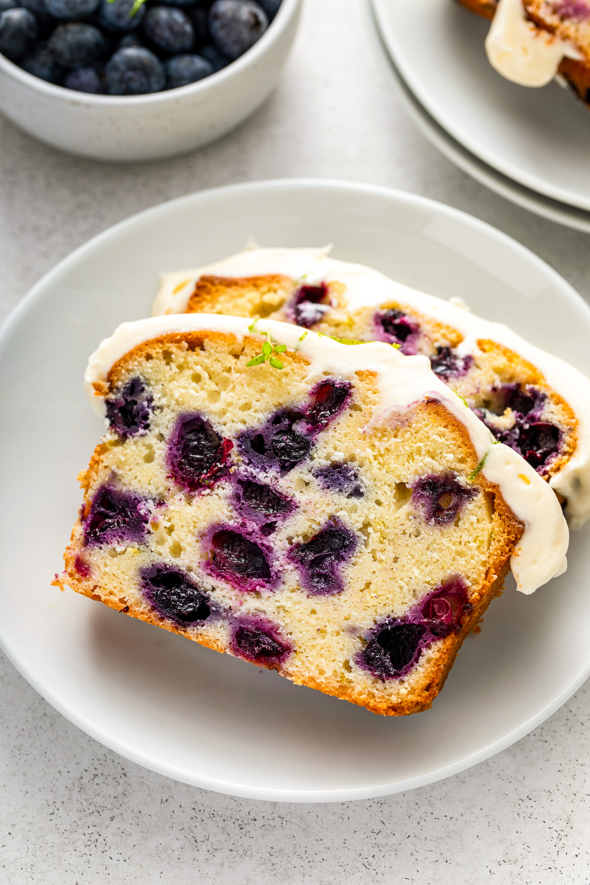 Two slices of lime blueberry pound cake with cream cheese frosting on top on a plate.