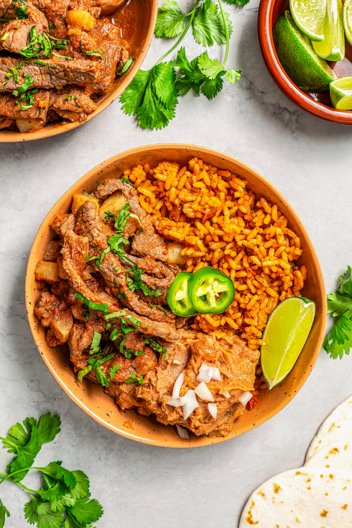 Steak ranchero served in a bowl with a side of yellow rice and refried beans.