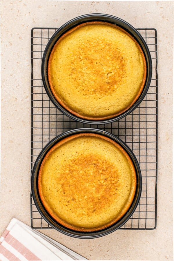 Two cakes baked in round pans cooling on a metal baking rack.