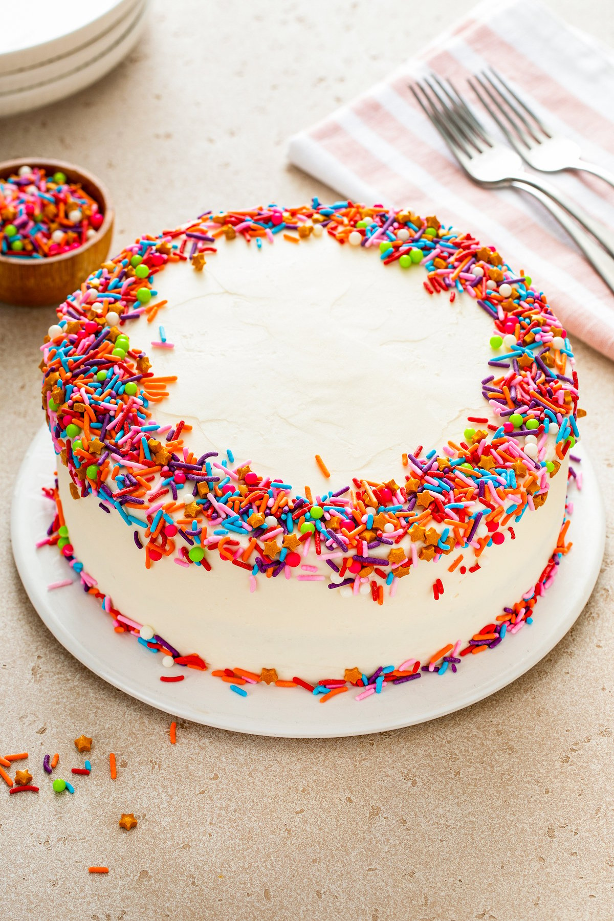A whole vanilla layer cake frosted and decorated with rainbow sprinkles.
