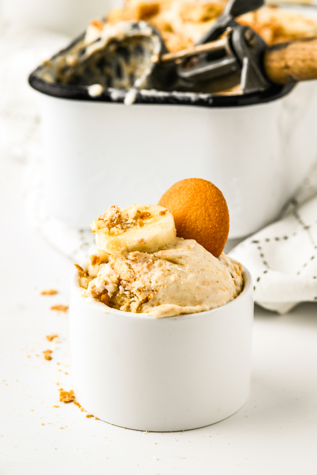 Ramekin with homemade banana pudding ice cream garnished with a nilla wafer and a slice of fresh banana.