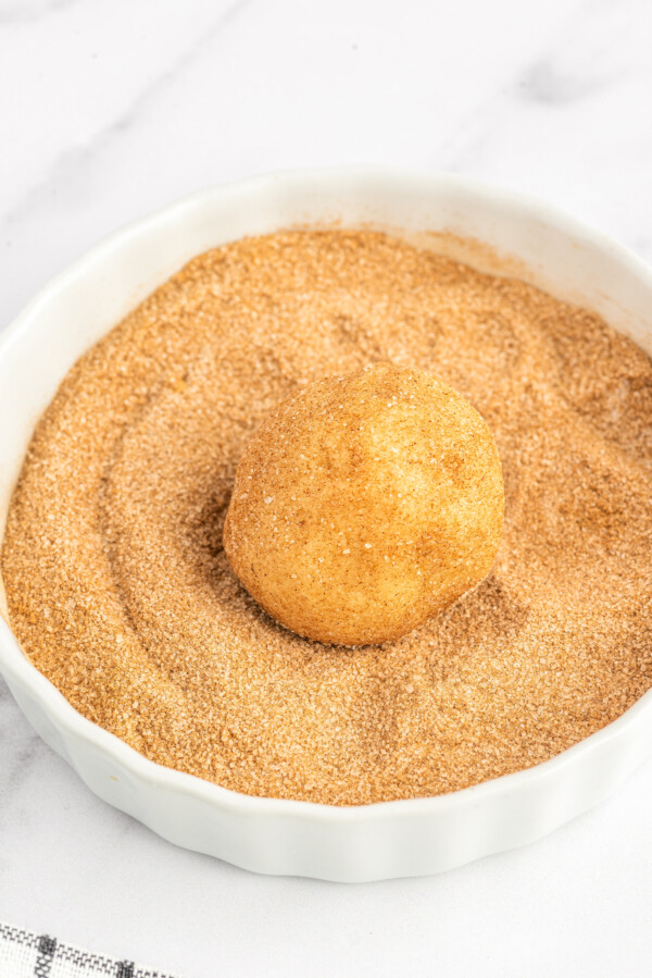 A cookie dough ball being coated in cinnamon sugar.