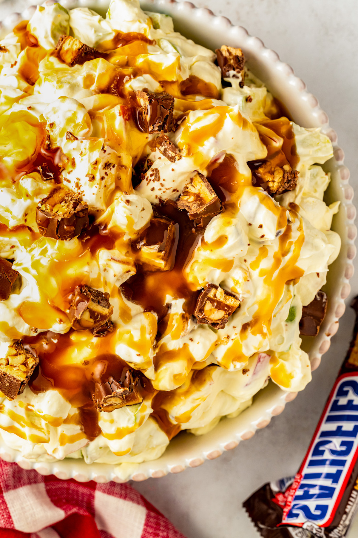 Sweet, creamy and chilled Caramel Apple Snickers Salad in a serving bowl with caramel sauce drizzled on top and a sprinkling of chopped snickers bars.