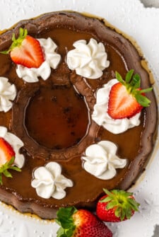 Whole flan with caramel on top, whipped cream swirls, and sliced strawberries.