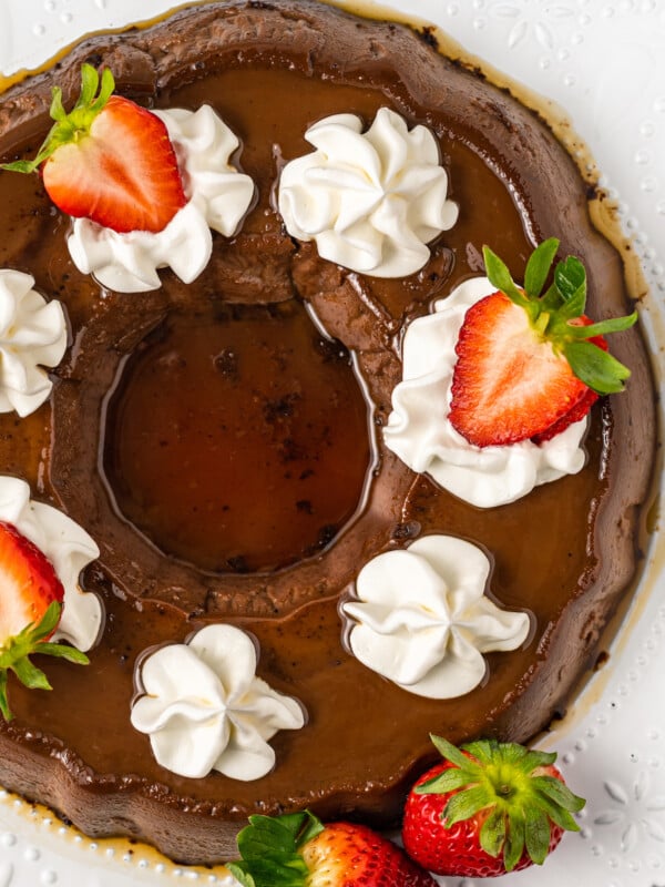 Whole flan with caramel on top, whipped cream swirls, and sliced strawberries.