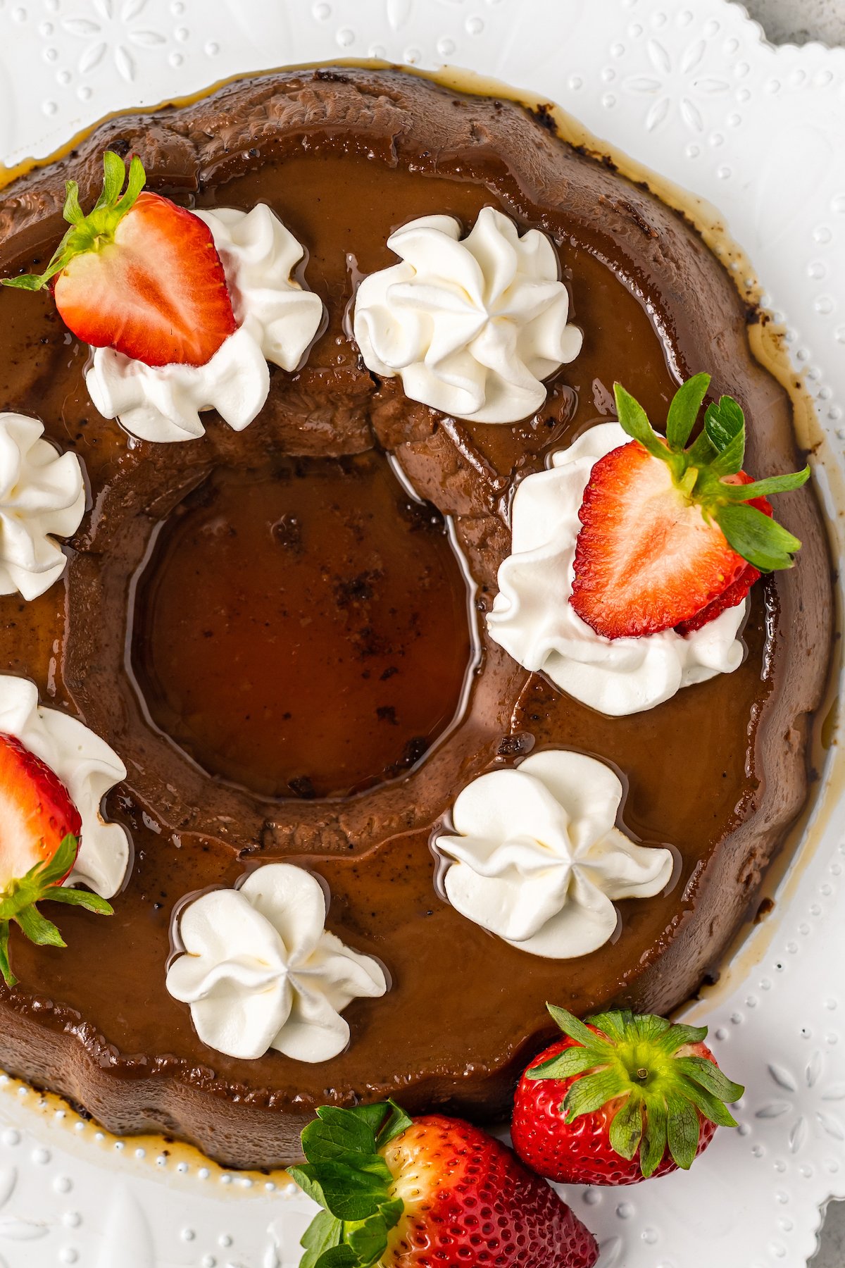 Whole chocolate flan topped with caramel sauce, whipped cream swirls, and sliced fresh strawberries. 