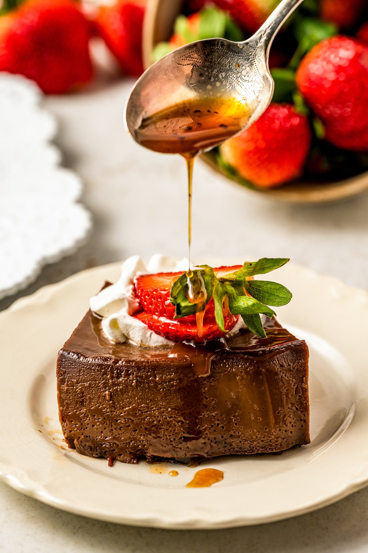 Drizzling caramel over a slice of chocolate flan with whipped cream and a sliced strawberry.