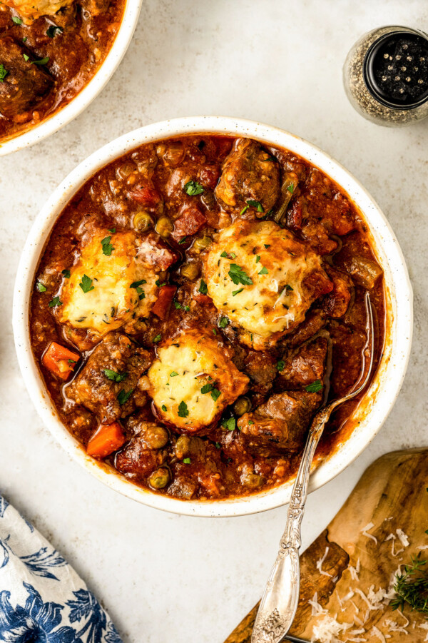 A bowl of hearty crockpot beef stew with dumplings in a rich brown gravy and a spoon ready to take a bite.