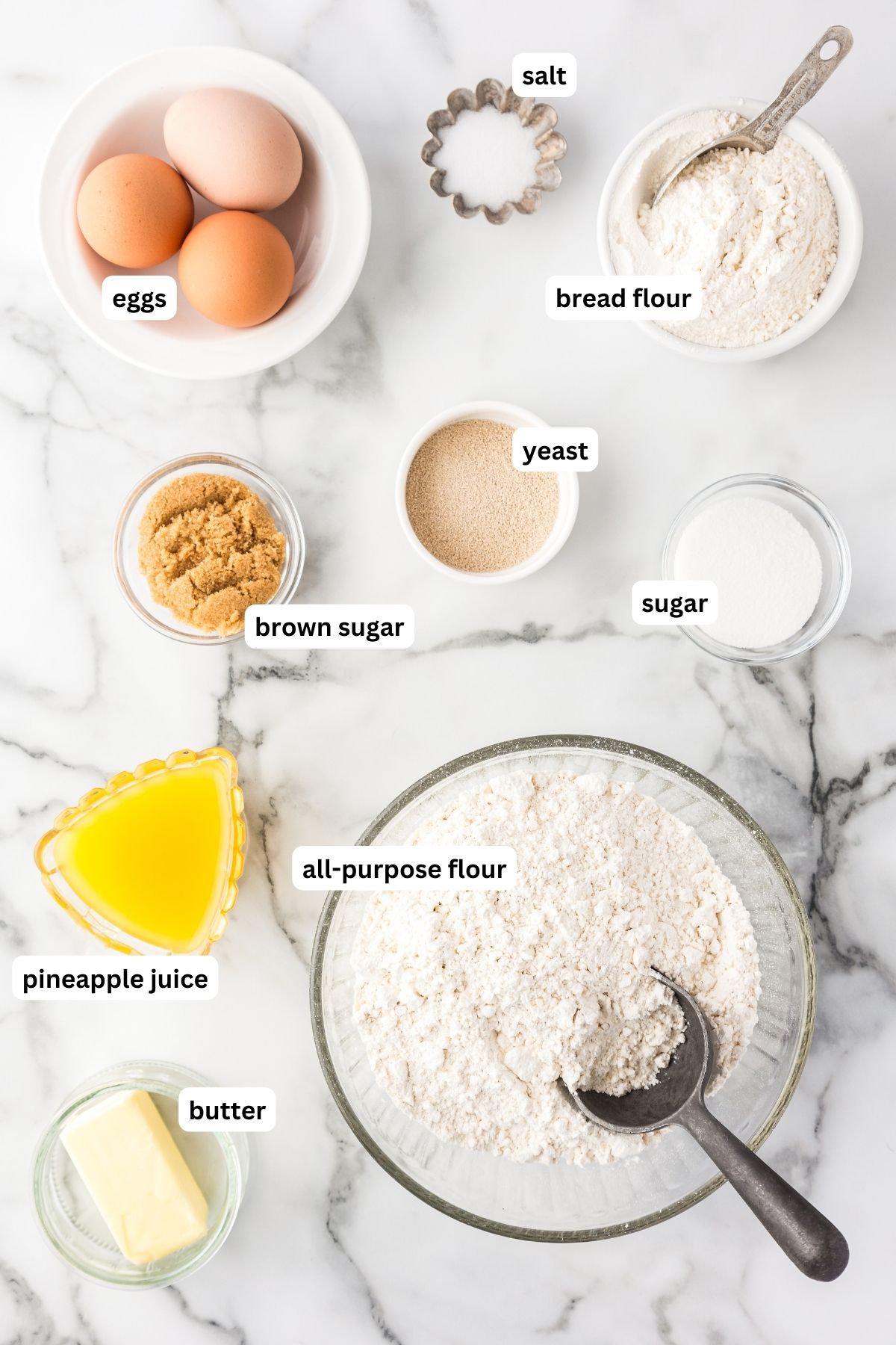 Hawaiian roll recipe ingredients arranged in bowls, from top to bottom: eggs, salt, bread flour, yeast, brown sugar, granulated sugar, pineapple juice, all purpose flour and butter.