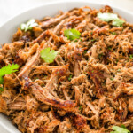 A bowl of juicy and crispy shredded instant pot carnitas topped with fresh cilantro.