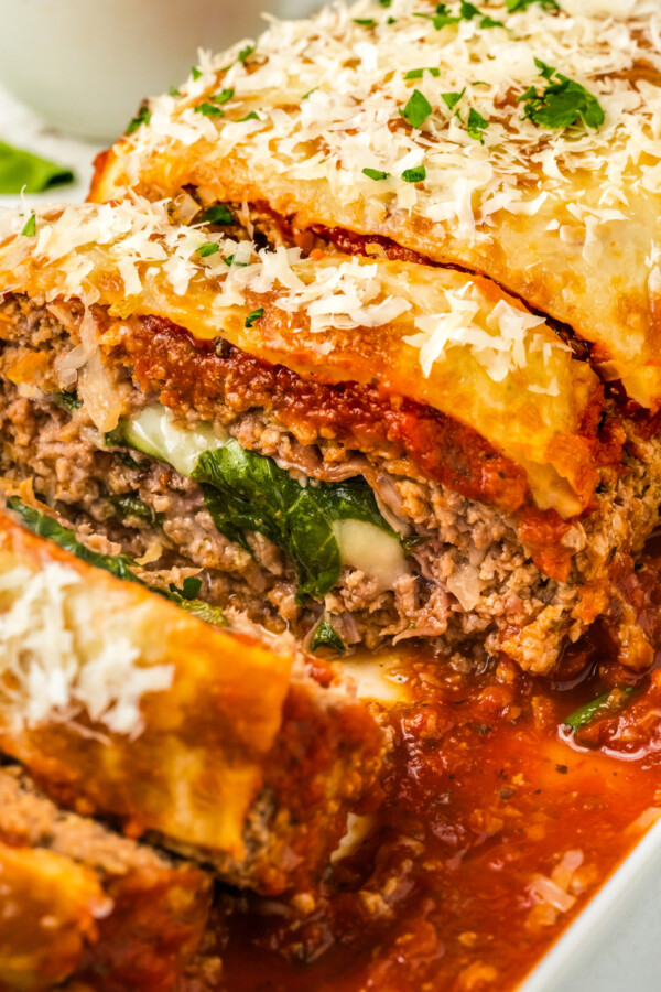 A juicy Italian stuffed meatloaf with cheese, spinach and prosciutto topped with marinara sauce, baked and sliced on a serving platter.
