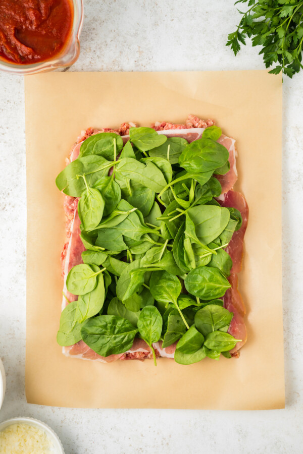 Flattened meatloaf mixture topped with prosciutto and baby spinach.