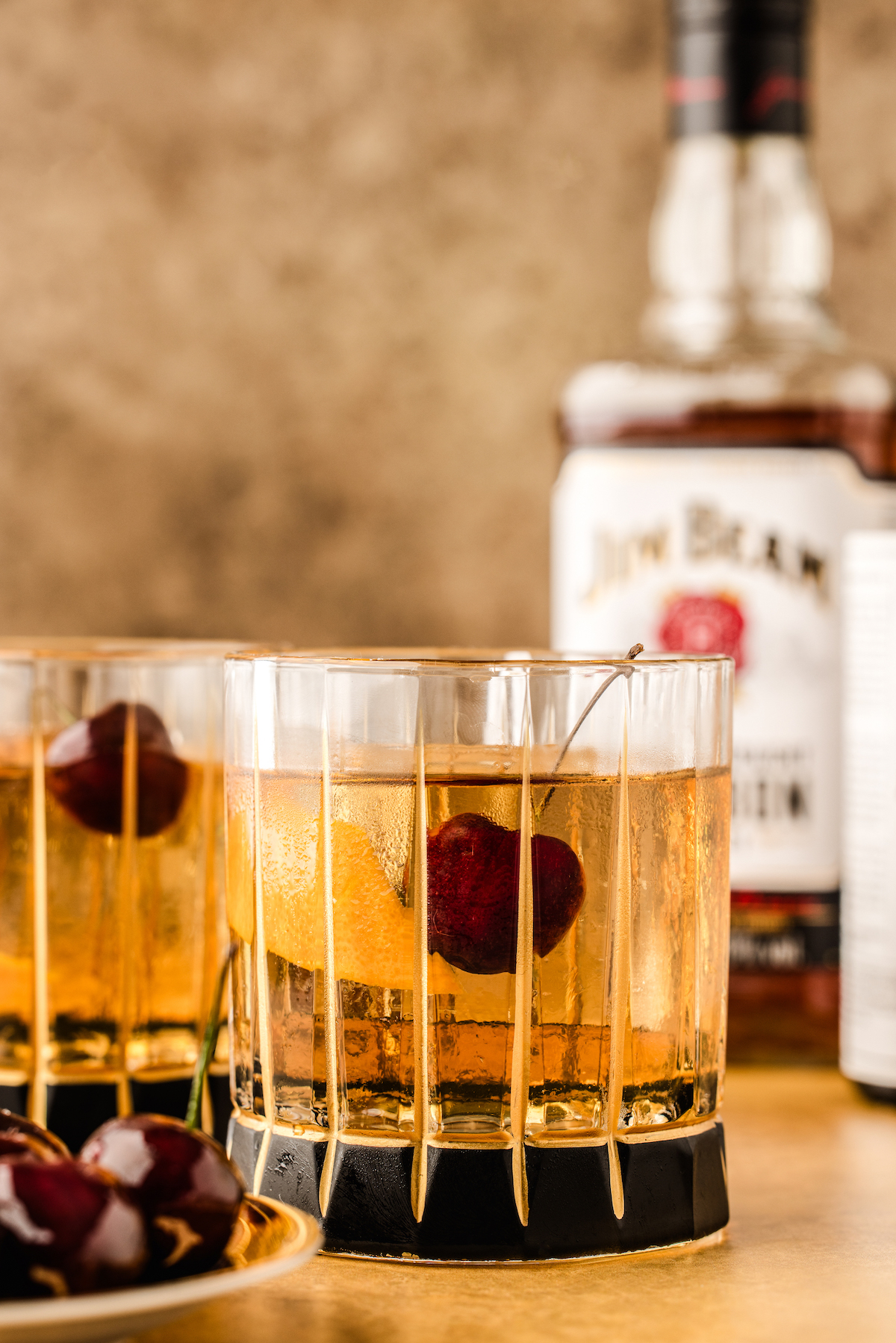 Old fashioned cocktail garnished with a succulent sweet cherry and an orange peel.