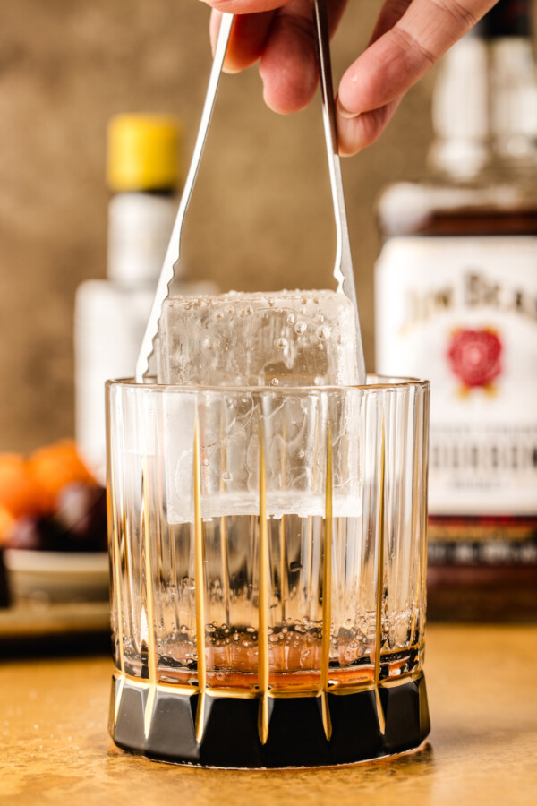 Adding the large single ice cube to the glass.