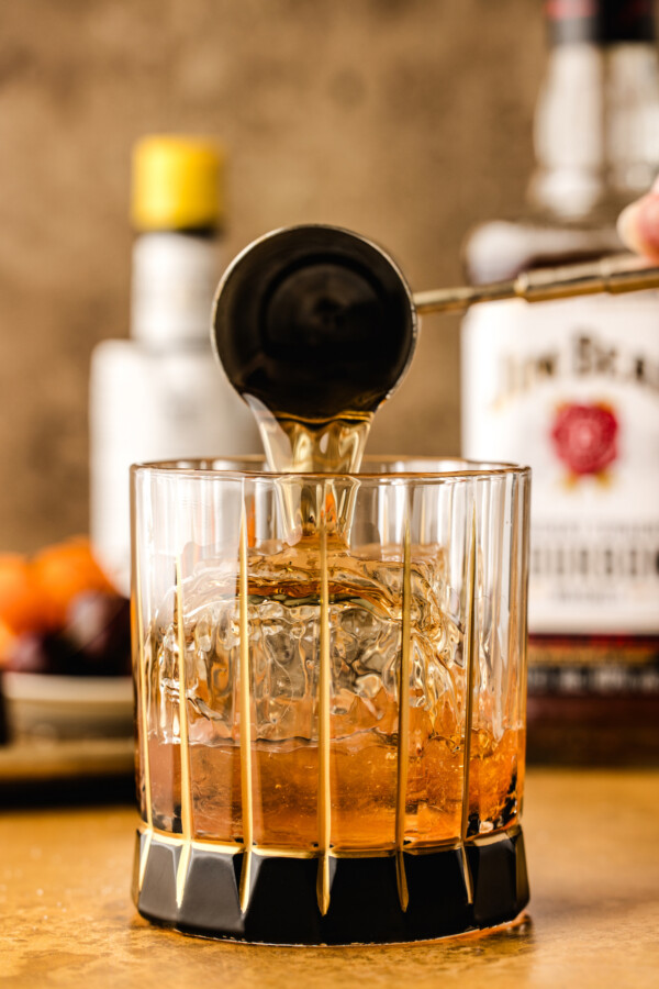 Pouring the bourbon into the short cocktail glass over the top of the large ice cube.