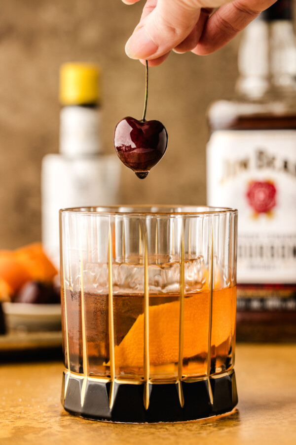 Garnishing the cocktail with a cherry and fresh orange peel.