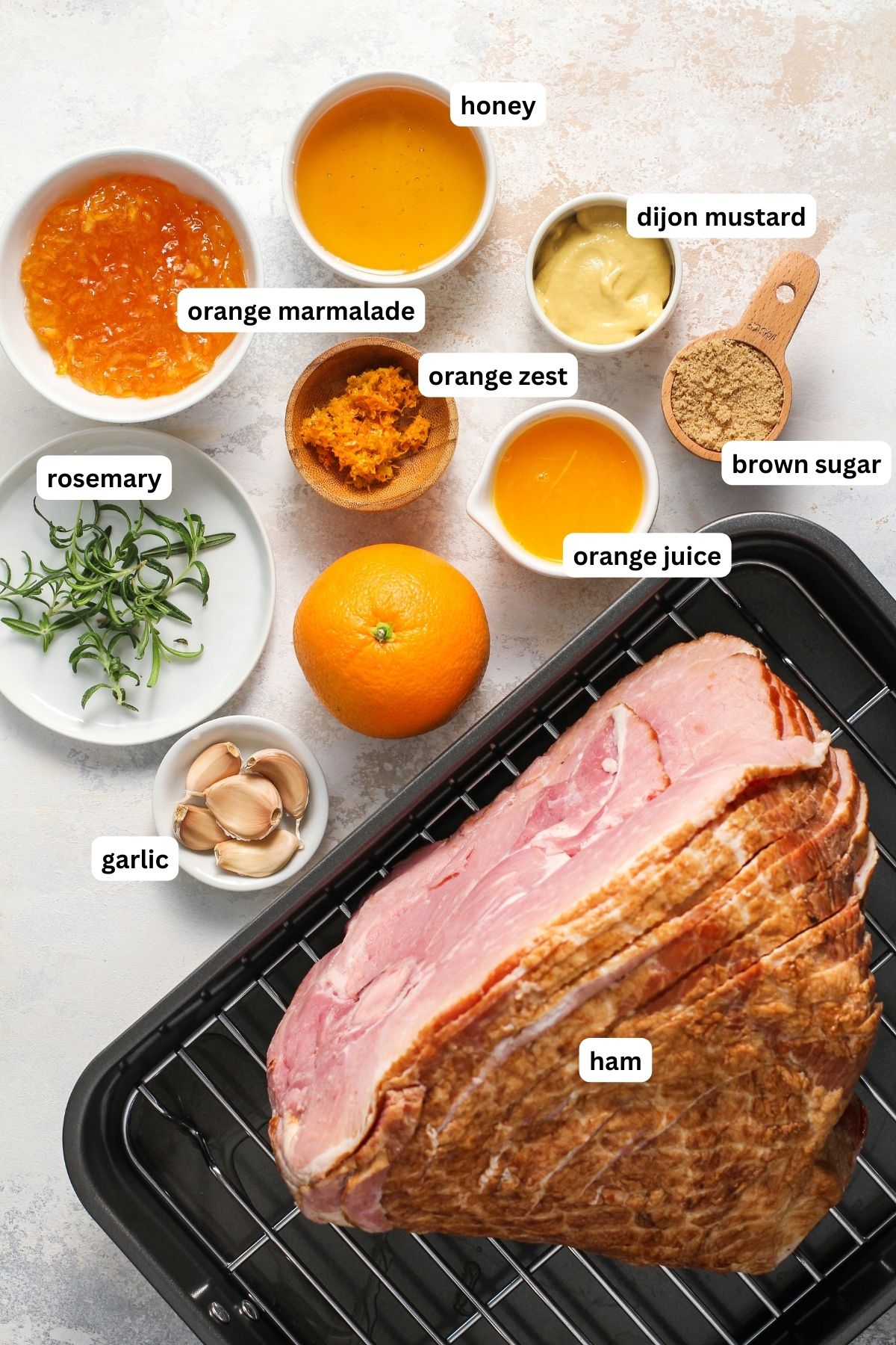 Orange glaze ham recipe ingredients arranged in bowls. From top to bottom: honey, orange marmalade, Dijon Mustard, orange zest, brown sugar, orange juice, rosemary, garlic and a spiral ham.