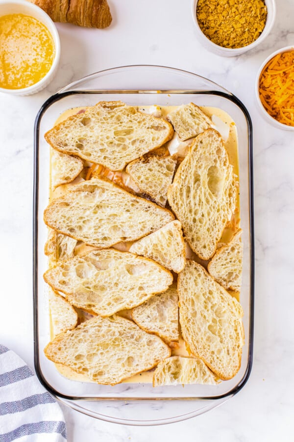 Sliced croissants being layered on top of whisked eggs, ham and cheese.