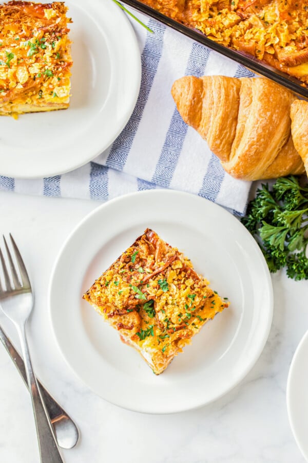 Two plates filled with slices of overnight breakfast casserole with ham with forks on the side.