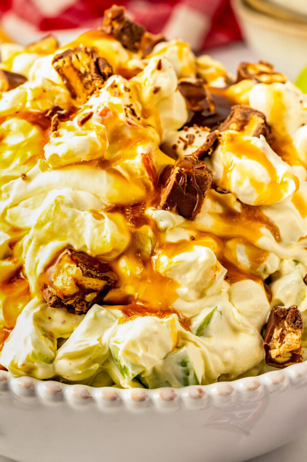 Sweet and creamy Snickers Apple Salad in a bowl topped with caramel sauce and more chopped snickers bars.
