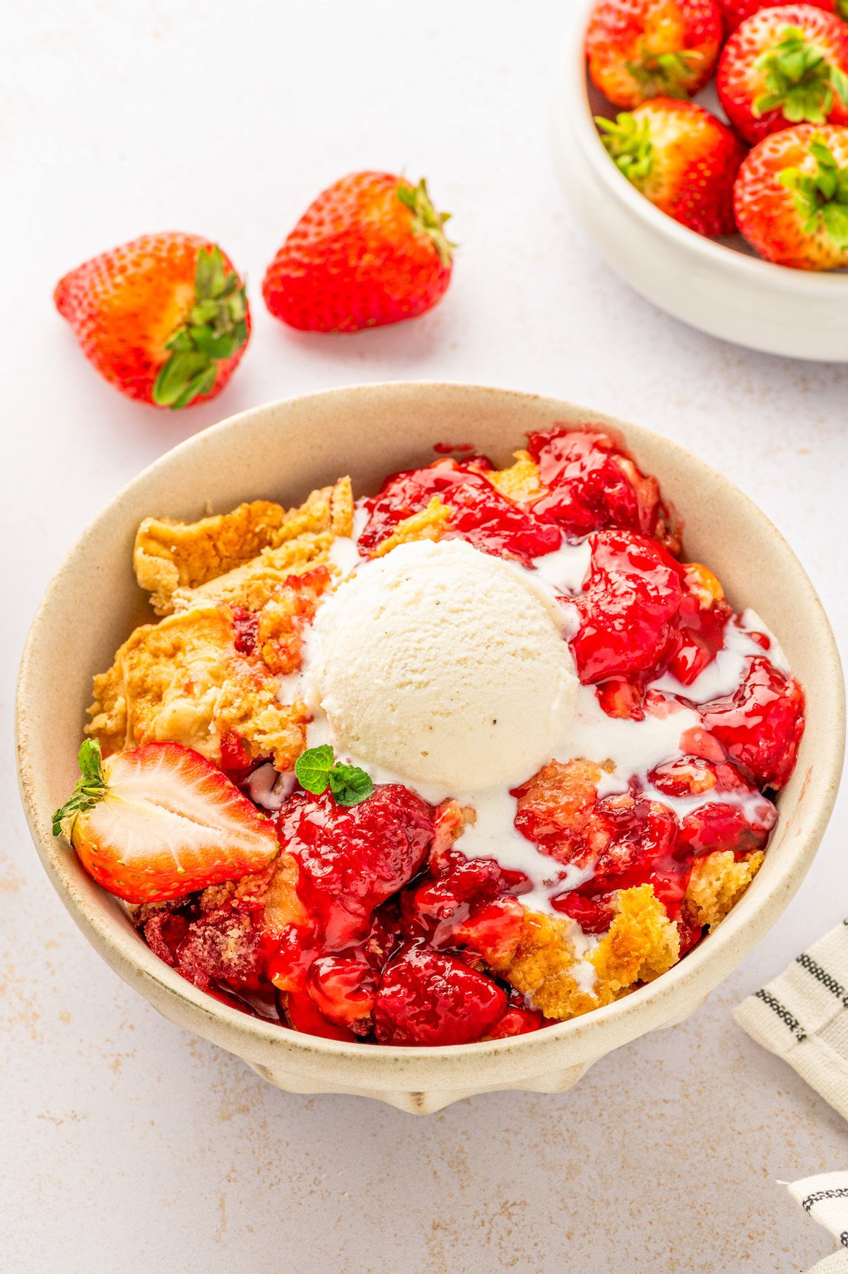 A warm strawberry cake made easy with a box of cake mix is served in a bowl topped with a scoop of vanilla ice cream.