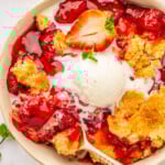A bowl of warm strawberry dump cake with a scoop of vanilla ice cream on top with a fork taking a bite.