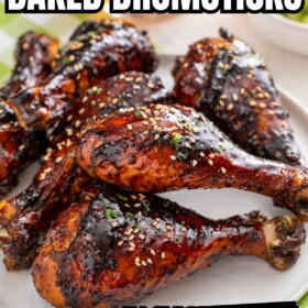 Sweet and sticky baked chicken drumsticks on a plate topped with sesame seeds and fresh herbs.