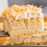 A slice of moist coconut poke cake being served with a cake serve out of a baking pan.