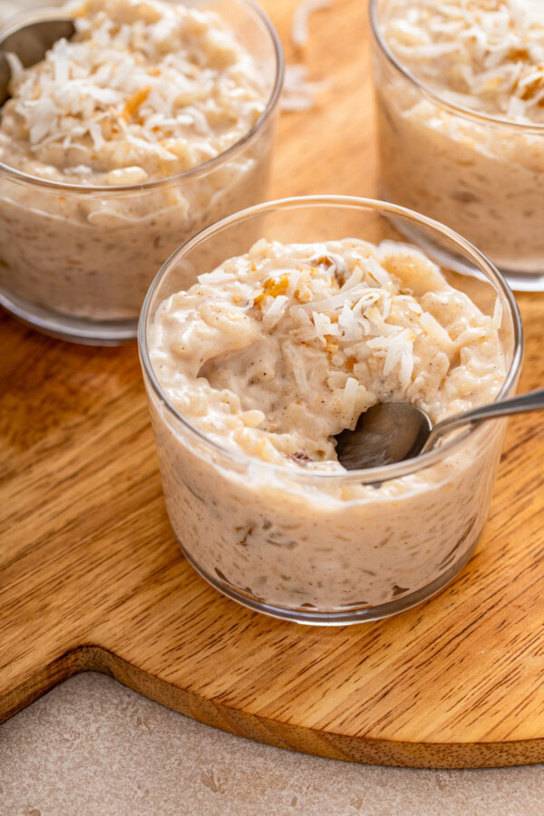 Three bowls of coconut milk rice pudding topped with toasted shredded coconut with one bowl half eaten with a spoon in it.