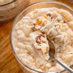 A bowl of creamy coconut rice pudding with golden raisins and topped with toasted coconut with a spoon taking a bite.